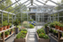 “High-resolution photo of a modern aluminum greenhouse in a landscaped backyard, interior view showing raised garden beds, potted plants, and natural light, clean architectural design, soft daylight, realistic residential setting.”